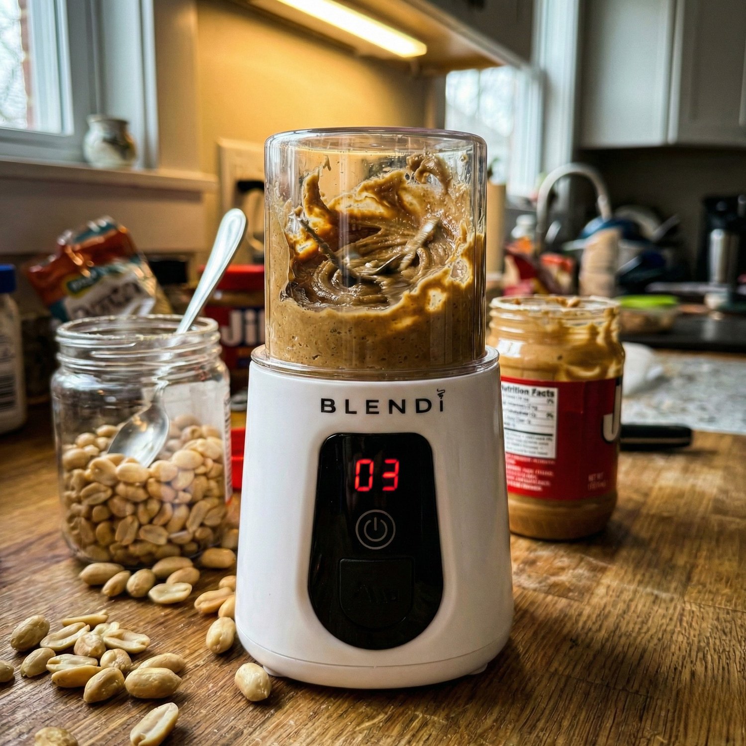 A jar of homemade nut butter on a kitchen table with ingredients nearby.