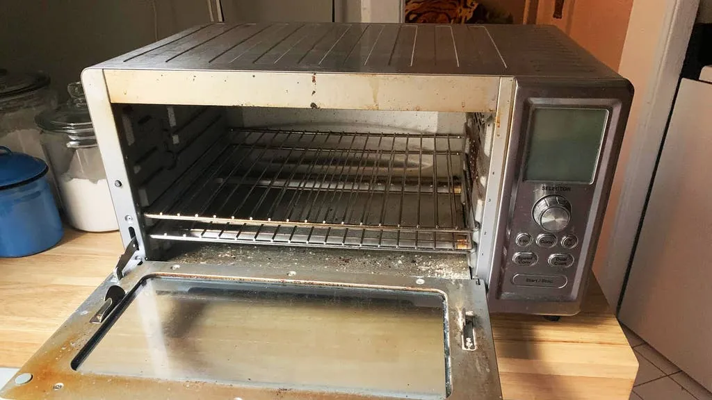 Hand in a glove wiping the inside of a compact toaster oven